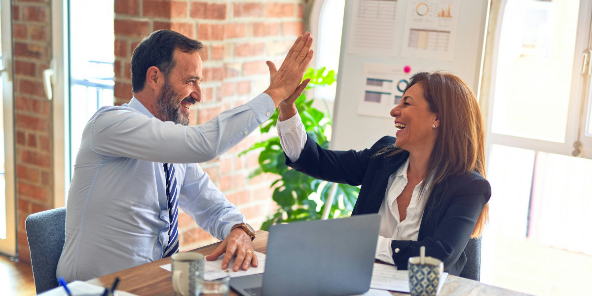 Mann und Frau im Business-Outfit geben sich im Büro ein High-Five als Zeichen erfolgreicher Zusammenarbeit